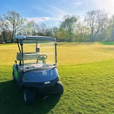 A golf cart traveling on a course near a putting green.