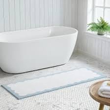 A bath mat on the floor beside a bathtub.