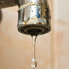 Water drops falling from a leaking household faucet.