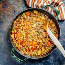 Green peas visible among the ingredients in a bowl of stew.