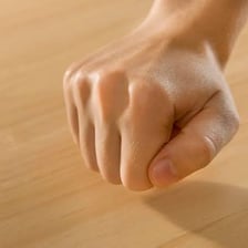 A hand knocking on a wooden table as a good-luck gesture