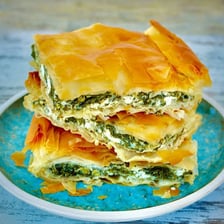 A block of feta cheese beside a slice of spanakopita