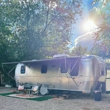 A person standing beside a polished silver Airstream travel trailer.