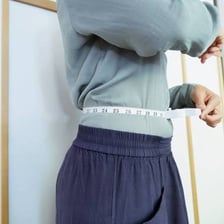 A person measuring their waist with a tape measure