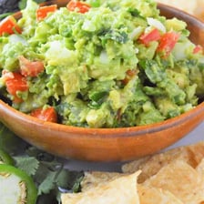 A bowl of green guacamole with avocado and chips
