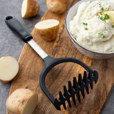 A potato masher crushing cooked potatoes into a pulp.