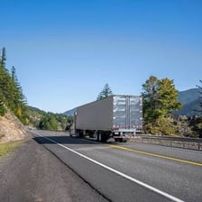 A trucker drives a large semi-truck on a long highway journey.