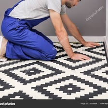 A worker installing carpet across a room floor.