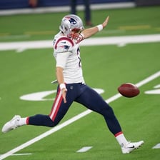 A football punter in a Patriots uniform kicking the ball.