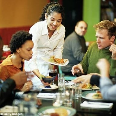 A restaurant server attending to diners at a table.