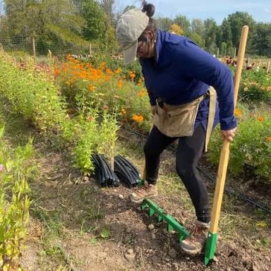 A gardener turns and loosens soil in a garden bed.