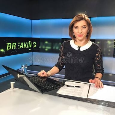 Television presenters sit at a desk in a news studio.