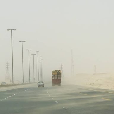 A vehicle traveling on a desert highway through blowing dust with severely reduced visibility