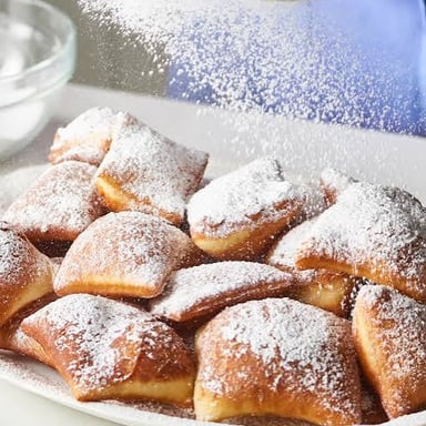 A fried beignet topped with powdered sugar.