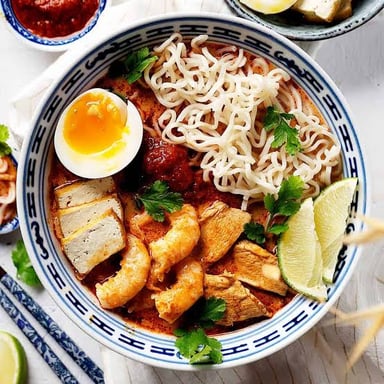 A bowl of laksa with noodles in a spiced broth.