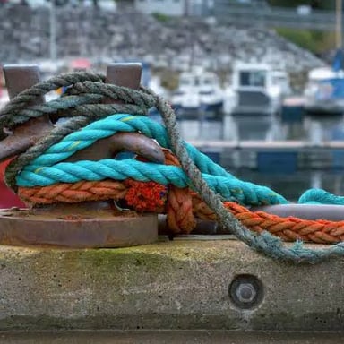 A boat’s rope is secured to a short bollard on a dock.