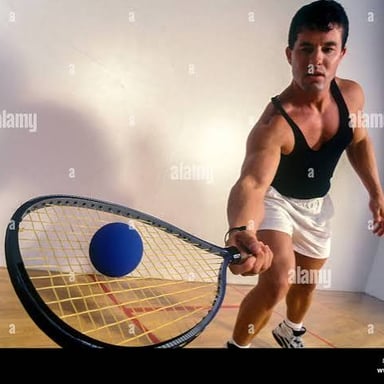 A player striking a ball with a racquet inside an enclosed racquetball court.