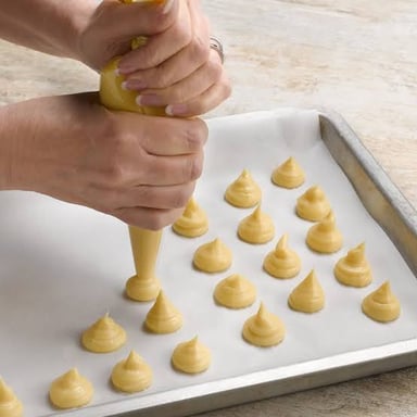 Choux pastry dough piped into small portions on a baking tray.