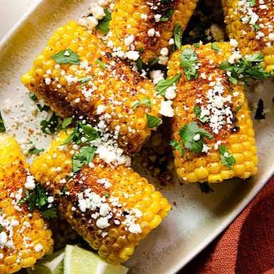 Grilled corn on the cob dressed with creamy sauce, cheese, chile, and lime.