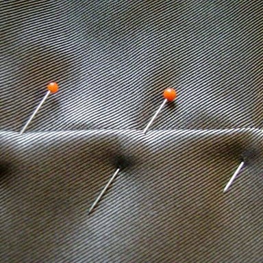 A tailor pinning fabric on a garment to adjust its fit.