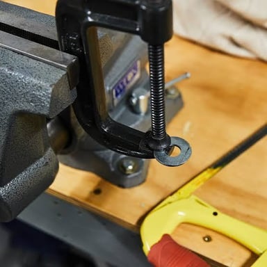 A C-clamp tightened around a piece of wood on a workbench.