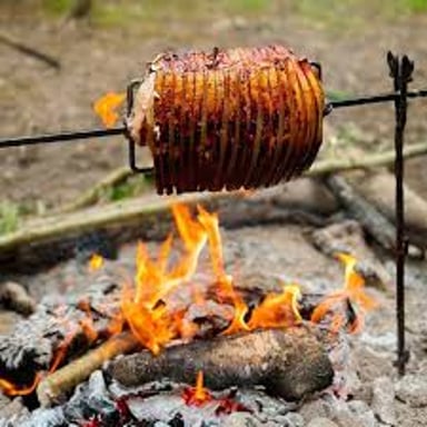 Meat rotating on a spit above a fire as it cooks.