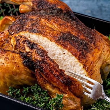 A chicken cooking in a roasting pan in an oven.