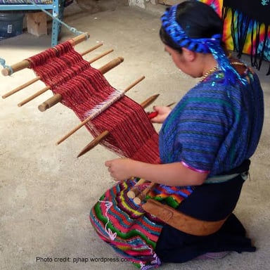 A weaving loom holding lengthwise warp threads and woven cloth.