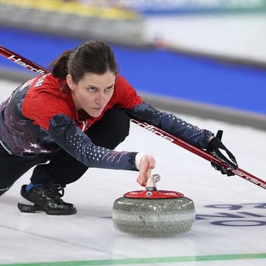 A granite curling stone on the ice, aimed toward the circular target rings.