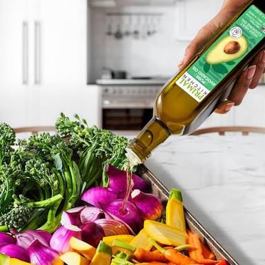 Avocado oil in a bottle beside a bowl of avocados.