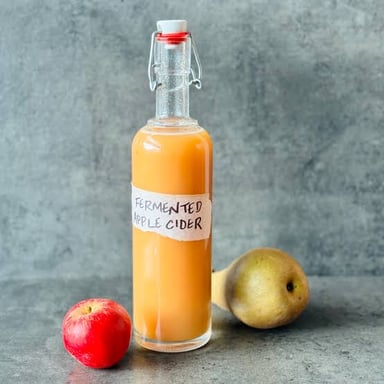 A glass of cider beside fresh apples.