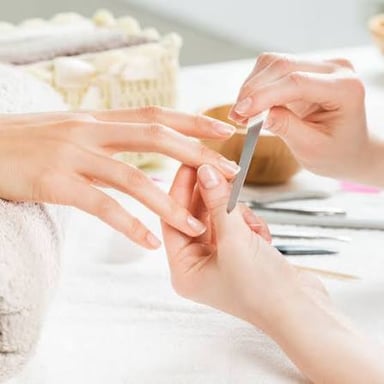 A nail technician filing a client's fingernails during a manicure.