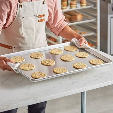 A baker holding metal baking pans in a bakery.