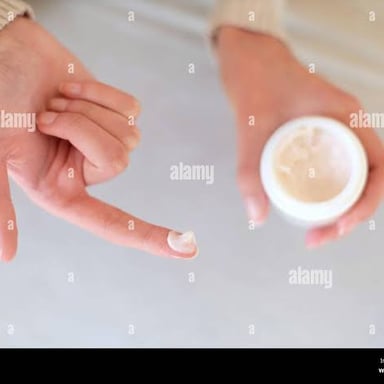 A fingertip lightly applying a small amount of lotion to skin.