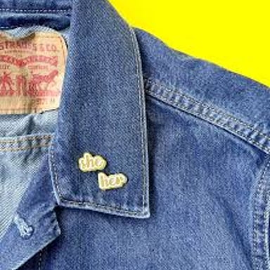 A pin displaying the pronouns she/her.