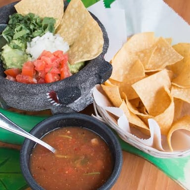 A hand dipping a tortilla chip into a shared bowl of salsa.