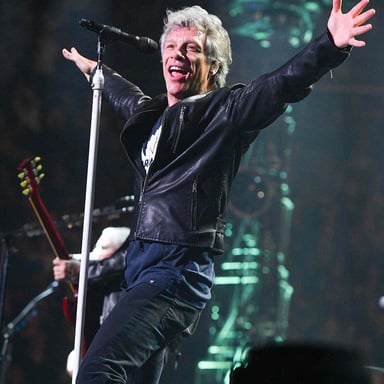 Jon Bon Jovi performing with a microphone at a rock concert.