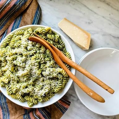 Green basil pesto sauce sits in a bowl beside pasta.