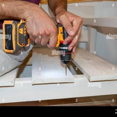 A carpenter using a cordless drill to make a hole in a wooden board