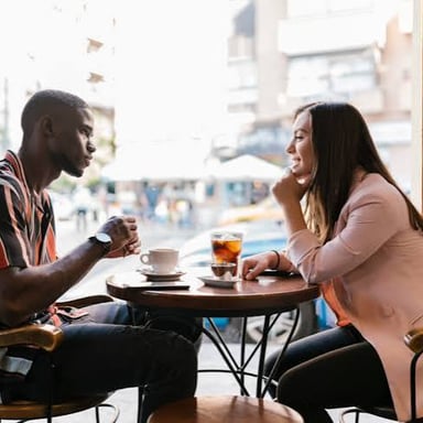 Two people exchange playful expressions while talking in a café.