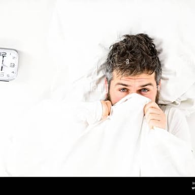 A person relaxing in bed under the covers in the morning.