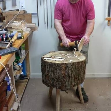 A woodworker chopping a tree trunk with an axe