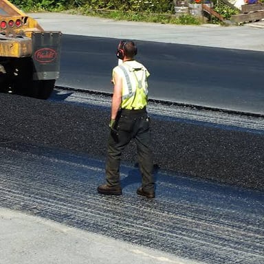 Workers paving a street with dark road surfacing material.
