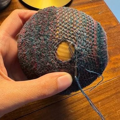 A hand uses a needle and thread to darn a hole in a sock.