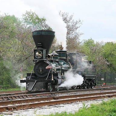 A steam locomotive with steam billowing as it sounds its whistle.