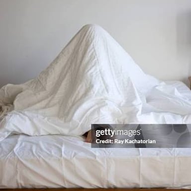 A person resting in bed beneath the covers.