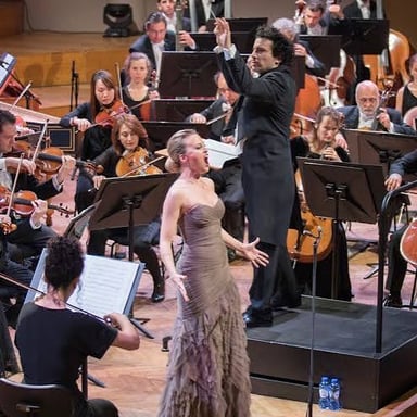A soprano singing on an opera stage with an orchestra accompanying her.