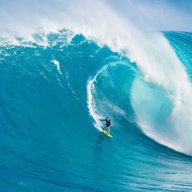 A surfer balancing on a board as an ocean wave breaks.