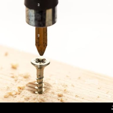 A screwdriver turning a threaded screw into a piece of wood.