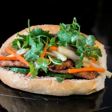 A Vietnamese bánh mì in a baguette with pickled vegetables and herbs.